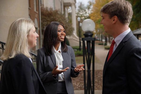 Three students have a discussion in front of Bidgood Hall